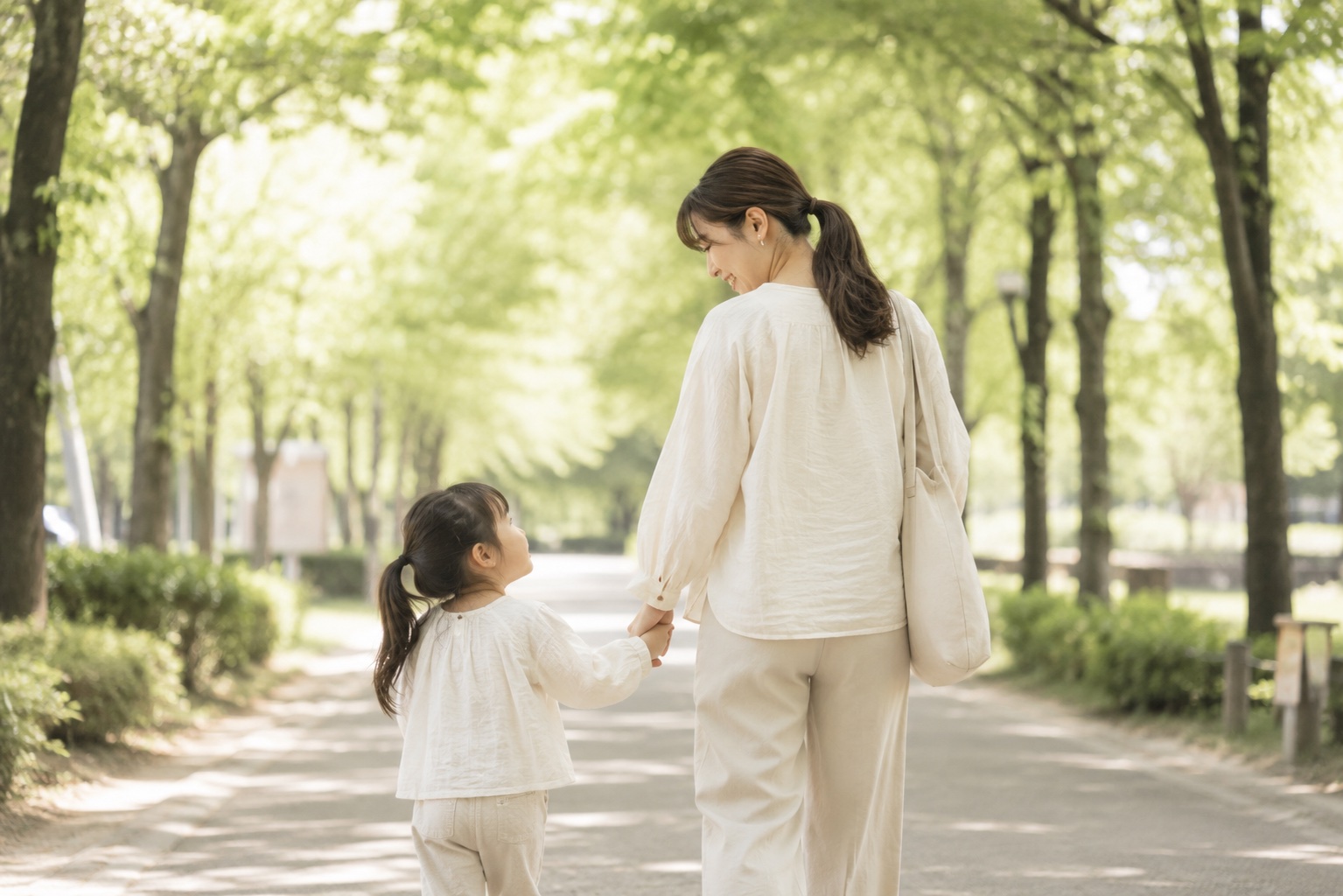 新緑の並木道で手をつないで歩くお母さんと上のお子さま